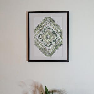 Peut inclure: Œuvre d'art encadrée avec un motif géométrique vert et blanc. Le motif en forme de losange présente des motifs et du texte complexes. Le cadre noir est accroché sur un mur blanc.