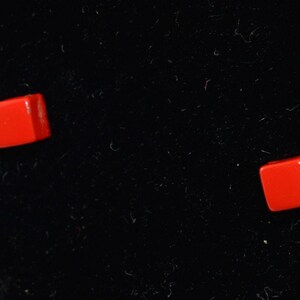 May include: Two small, red, square-shaped buttons on a black background.