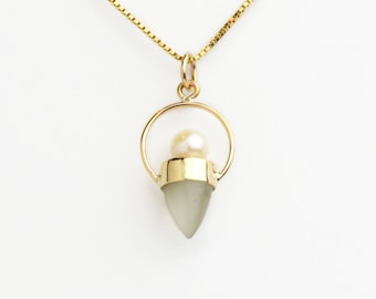 May include: A gold chain necklace with a pendant featuring a gray teardrop-shaped stone with a gold setting and a pearl inside a gold ring.