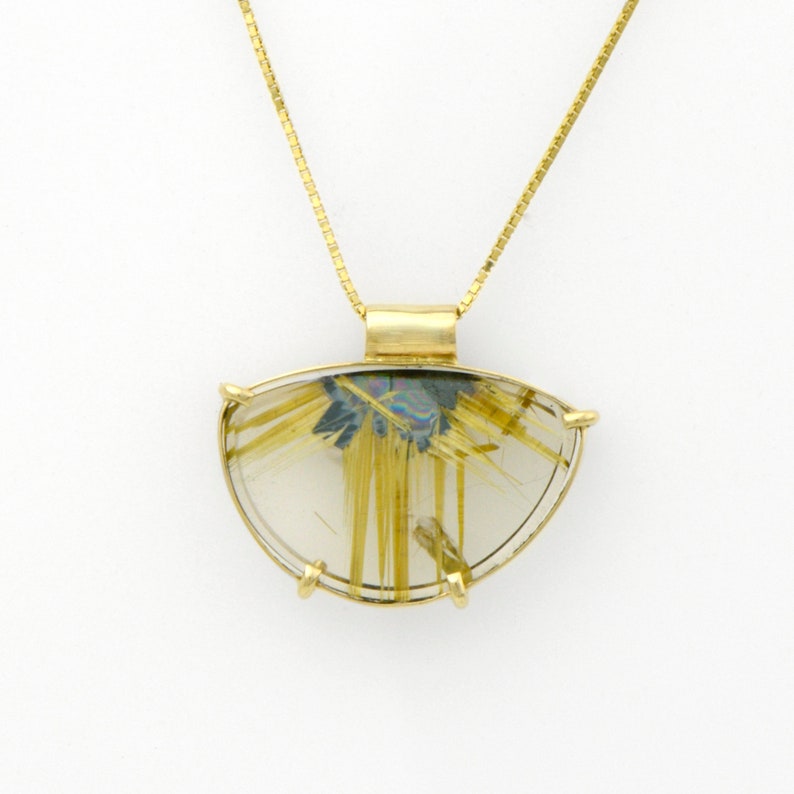 May include: A gold pendant necklace featuring a clear, semi-circular stone with gold-colored inclusions. The stone is set in a gold bezel and suspended from a delicate gold chain. The pendant has a unique, natural appearance.