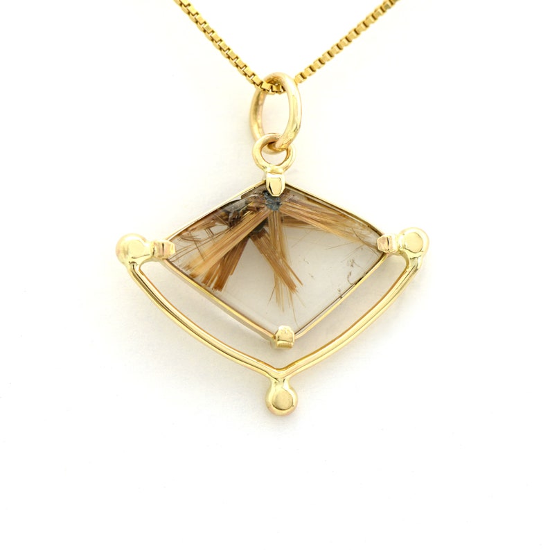 K&ouml;nnte beinhalten: Eine goldene Halskette mit einem Anh&auml;nger aus klarem Quarzkristall mit braunen Einschl&uuml;ssen. Der Kristall ist in einem goldenen Rahmen mit einer Diamantform gefasst. Der Anh&auml;nger h&auml;ngt an einer zarten goldenen Kette.