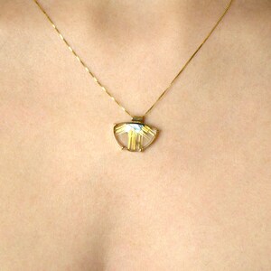 May include: A gold necklace with a pendant featuring a clear, semi-circular stone with gold-colored inclusions. The pendant is suspended from a delicate gold chain, creating a simple yet elegant design. The necklace is shown against a skin-toned background.