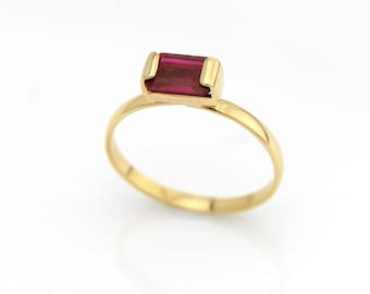May include: A gold ring with a single, rectangular, dark red gemstone.