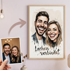 Pode incluir: Um retrato em aquarela emoldurado de um casal sorrindo, com o texto alemão "Lachen verbindet" (O riso conecta). A obra de arte está em uma moldura de madeira, e uma foto menor do casal é segurada em uma mão.