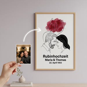 Puede incluir: Una impresión artística enmarcada con un dibujo lineal de una pareja, el número 40 y el texto "Rubinhochzeit Maria & Thomas 22. April 1983". Una pequeña foto se sostiene frente al arte. El arte tiene un fondo de acuarela.