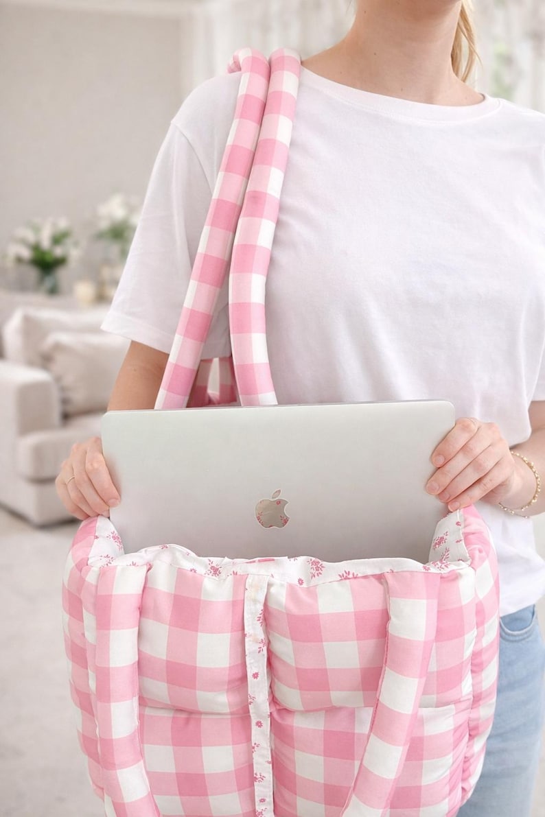 Może przedstawiać: R&oacute;żowa i biała torba typu tote w kratę z pasującymi, wyściełanymi paskami. Torba mieści srebrny laptop. Torba ma kwiatowe wykończenie i zapięcie na guziki. Torba jest przeznaczona do przenoszenia laptopa i innych niezbędnych rzeczy.