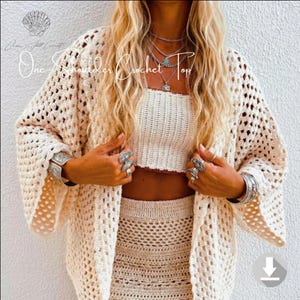 May include: Cream-colored crochet cardigan with open weave, paired with a matching crop top and skirt. The image features the text "One Shoulder Crochet Top". The outfit is accessorized with silver jewelry.