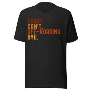 Könnte beinhalten: Dunkelgraues T-Shirt mit dem Text "SORRY. CAN'T. OFF-ROADING. BYE." in Orange und Gelb. Das T-Shirt hat einen Rundhalsausschnitt und kurze Ärmel.
