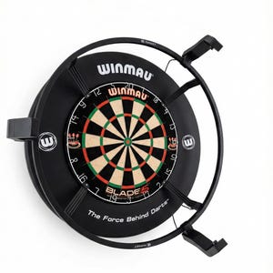 Op de afbeelding: Een zwart Winmau dartbord met een Blade 5 doel. Het dartbord heeft een klassiek ontwerp met rode, groene en bruine segmenten. De tekst "The Force Behind Darts" staat onderaan. Het is gemonteerd op een zwart metalen frame.