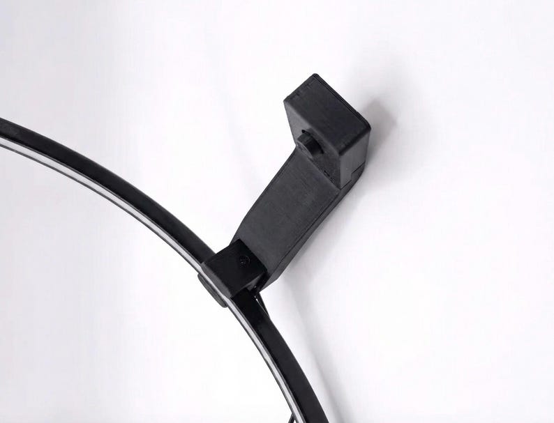 May include: A black, curved lamp with a white light strip. The lamp has a rectangular base and a connecting arm. The lamp is set against a white background.