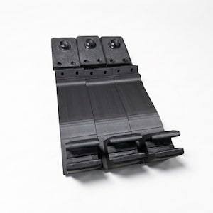 May include: A black, industrial component with three sections. Each section has a rectangular base with a curved top and small holes. The top features three raised circular elements. The component is set against a white background.