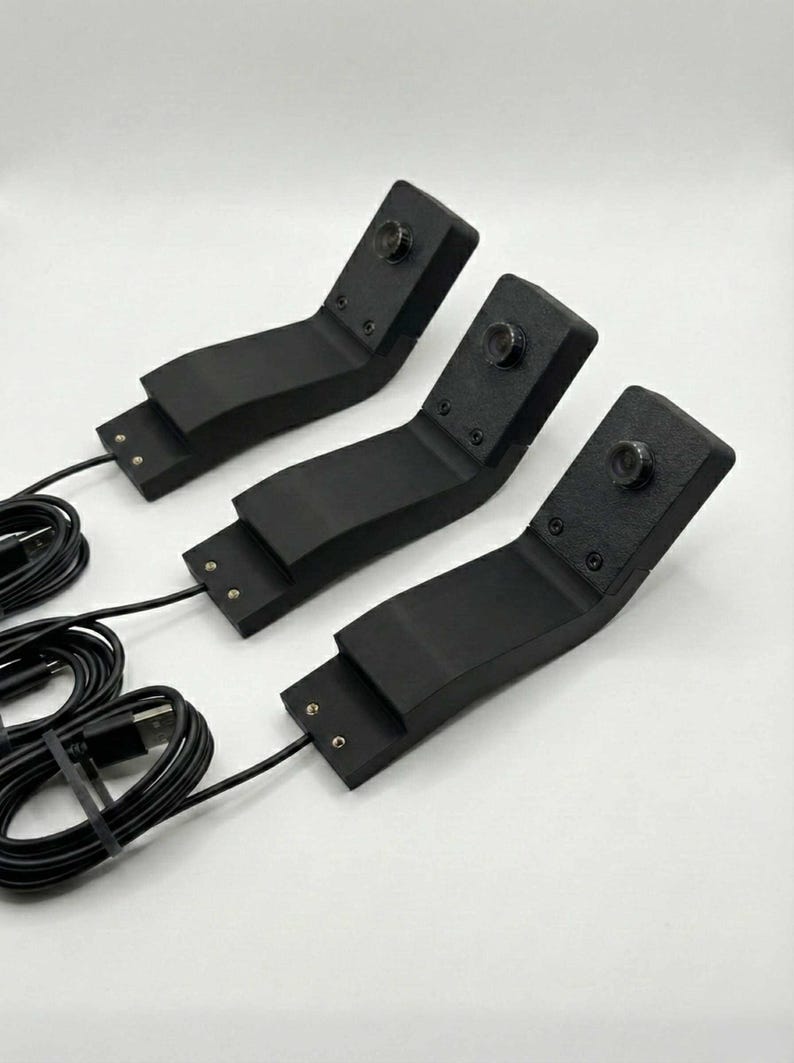 May include: Three black, angled devices with attached cables and USB connectors. Each device has a small, circular lens on the top angled section. The devices are arranged on a white surface.