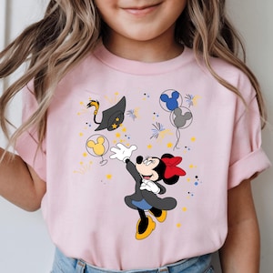 Peut inclure: T-shirt rose avec un motif de Minnie Mouse. Minnie tend la main vers une toque de graduation et des ballons. Le motif comprend des étoiles jaunes et des feux d'artifice. Le t-shirt a des manches courtes.