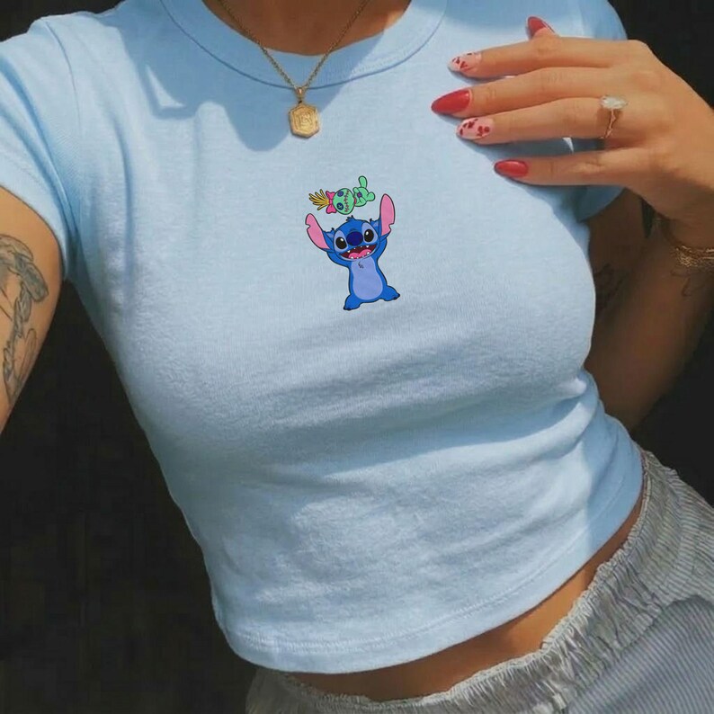 Peut inclure: Haut court bleu clair avec un dessin anim&eacute; de Stitch. Le haut a des manches courtes et un col rond. Le dessin de Stitch est dans les tons de bleu et de rose.