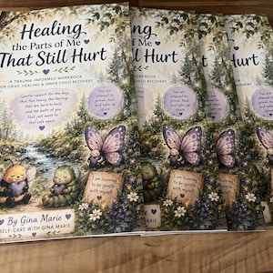 May include: A stack of identical workbooks titled Healing the Parts of Me That Still Hurt by Gina Marie. The cover features a robin, a bee, and a caterpillar in a forest setting with butterflies and text about trauma, grief, and inner child recovery.