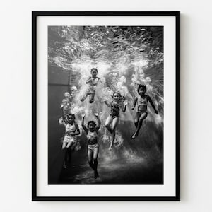 May include: Black and white framed photograph of children swimming underwater. Six children are captured mid-air, surrounded by bubbles, wearing swimsuits. The image is a study in motion and light.
