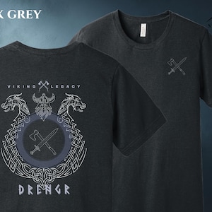 May include: Dark grey heather t-shirts with Viking-themed designs. One shirt features a front graphic with the text "VIKING LEGACY DRENGR" and a Viking emblem. The other shirt has a small axe and sword graphic. "SPLIT ROCK APPAREL" is printed on the top right.