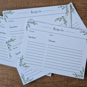 May include: Several white recipe cards with spaces for ingredients and directions. Each card features a green floral corner design and the words "Recipe for" at the top. The cards are stacked.