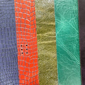 May include: A close-up of various textured leather samples in shades of brown, blue, red, gold, green, and black. The textures include embossed floral patterns, crocodile scales, and smooth finishes. The red sample has several punched holes.
