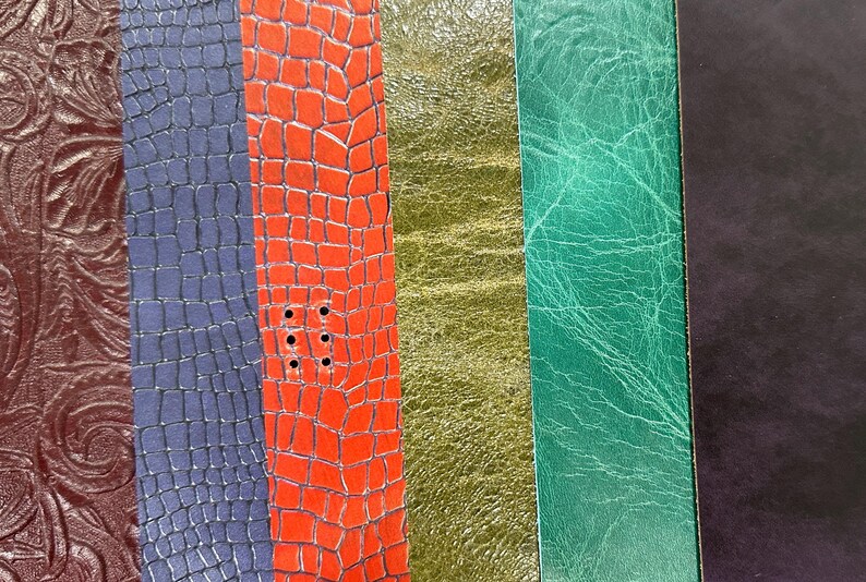 May include: A close-up of various textured leather samples in shades of brown, blue, red, gold, green, and black. The textures include embossed floral patterns, crocodile scales, and smooth finishes. The red sample has several punched holes.