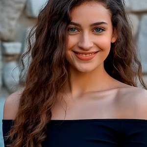 May include: A person with long, wavy brown hair and blue eyes smiles, wearing a black off-the-shoulder top. The background is a stone wall, creating a contrast with the subject's features.
