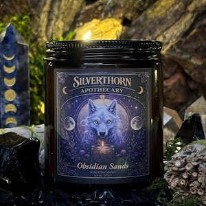 Puede incluir: Una vela en frasco de vidrio ámbar oscuro con tapa de rosca negra. La etiqueta presenta una ilustración morada y azul de un lobo, una vela pequeña y fases lunares, con el texto Silverthorn Apothecary, Obsidian Sands y 193g.