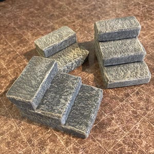 May include: Gray miniature stone steps, perfect for a fairy garden or model railroad. The steps are made of a textured material, with a weathered appearance. The set includes multiple individual steps.