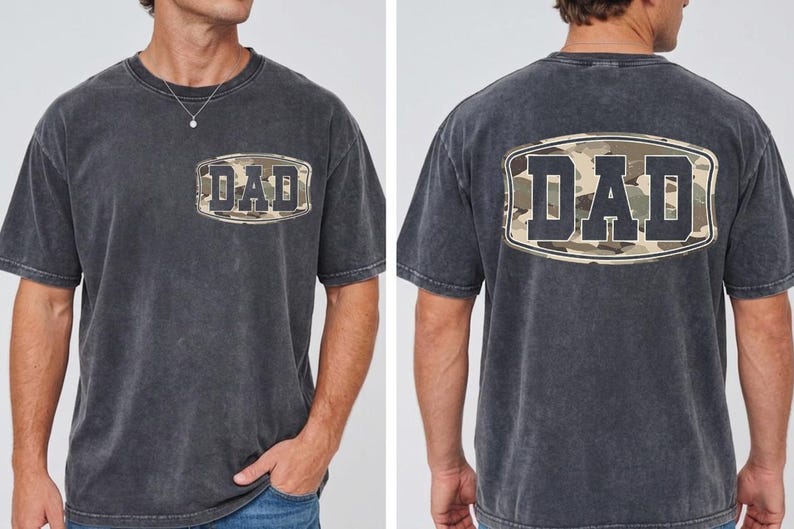 May include: Dark gray t-shirt with a camouflage design and the word "DAD" printed on the front and back. The shirt has a classic crew neck and short sleeves, perfect for casual wear.