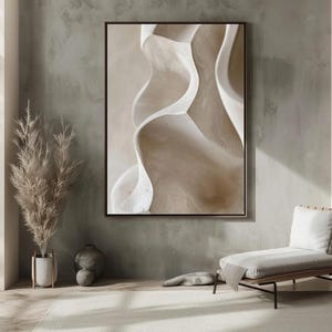 May include: Abstract art print with flowing beige and white shapes against a neutral backdrop. The artwork, framed in black, hangs above a modern chair and rug, creating a serene interior design.