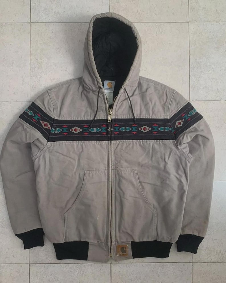 Puede incluir: Chaqueta con capucha gris claro con un dise&ntilde;o negro y estampado en el pecho. La chaqueta tiene una cremallera completa, dos bolsillos delanteros y pu&ntilde;os y dobladillo negros. La capucha est&aacute; forrada con tela negra.