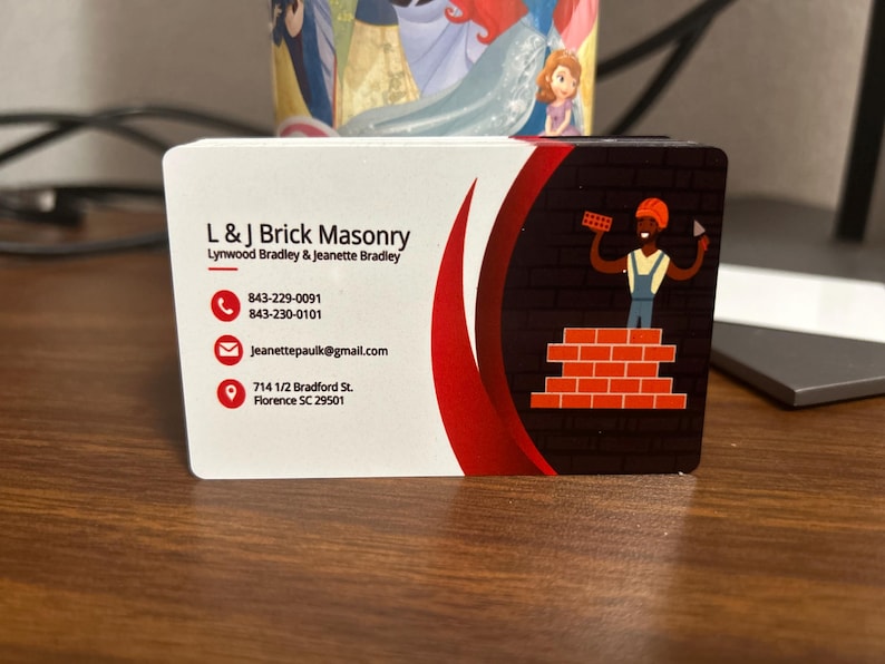 May include: A business card for L & J Brick Masonry, featuring the company name, contact information, and a graphic of a bricklayer. The card has a white background with a red curved design and a brick wall illustration.