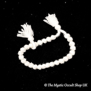Könnte beinhalten: Weißes Perlenarmband mit Quasten an beiden Enden, vor schwarzem Hintergrund. Das Armband besteht aus kleinen, runden Perlen und geknoteter Schnur. Unten steht „The Mystic Occult Shop UK“.