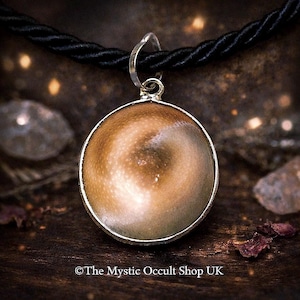 Puede incluir: Un colgante redondo con un marco plateado y un centro arremolinado marrón claro y blanco, suspendido de un cordón negro. El colgante tiene un aspecto brillante y pulido. El texto "The Mystic Occult Shop UK" está en la parte inferior.