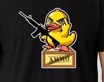 May include: Black t-shirt with a cartoon yellow duck illustration. The duck is holding a rifle and giving the middle finger. It sits on a wooden crate with the word "AMMO".