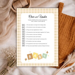 May include: A baby shower game card with a light yellow gingham pattern background. The card features the text "Over or Under" and a list of questions. The word "BABY" is spelled out in colorful letters at the bottom.
