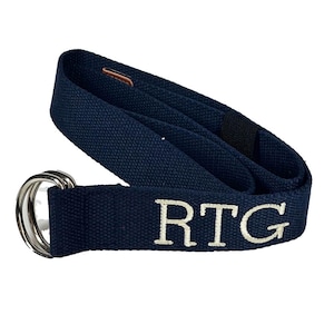 May include: A navy blue canvas belt with a silver double-ring buckle. The belt features the embroidered letters "RTG" in white. The belt is made of a durable fabric and has a leather accent near the end.