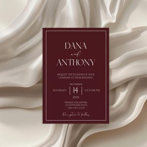 May include: A rectangular wedding invitation card in deep burgundy with white serif and script text. The card reads DANA and ANTHONY, REQUEST THE PLEASURE OF YOUR COMPANY AT THEIR WEDDING, SATURDAY DECEMBER 14 2025 AT 07:00 PM, VENUE LOCATION, and Reception to follow.