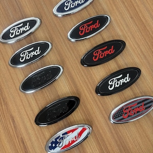 May include: A white ceramic mug with a black handle and the text "But First, Coffee" in a bold, black font. The mug is set against a blurred background, suggesting a cozy setting.