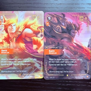 May include: Two collectible trading cards featuring a character named Sett, labeled as a Brawler. The cards display vibrant illustrations of the character in action, with text describing game mechanics and quotes.