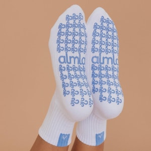 May include: A pair of white socks with blue accents. The soles feature a repeating blue pattern and the word "almla". The socks have a ribbed cuff and a small blue triangle near the ankle.