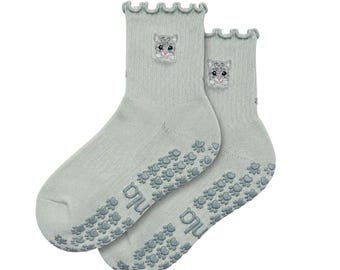 May include: A pair of sage green ankle socks featuring a ruffled top edge and an embroidered kitten face on the cuff. The soles are covered in a repeating pattern of small, gray, paw-shaped silicone grips and the text "nu" printed in gray.