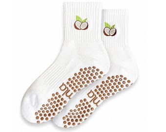 May include: A pair of white crew-length socks featuring an embroidered coconut graphic on the ribbed cuff. The soles are covered in brown circular silicone grip dots and include the text "nla" printed in brown on the arch area of each sock.