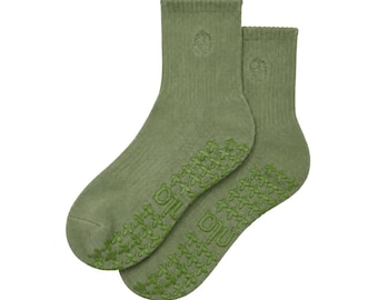 May include: A pair of olive green ankle socks featuring a ribbed texture and a small embroidered emblem on the upper cuff. The soles are covered in a repeating pattern of small, dark green cross-shaped silicone grips for added traction.