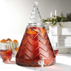 May include: A clear glass beverage dispenser shaped like a Christmas tree, filled with a red liquid and fruit slices. The dispenser has a star on top and a silver spigot. Two glasses of the red beverage are in front of the dispenser.