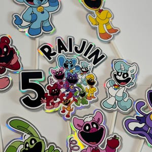 May include: A collection of colorful cartoon character cake toppers, including bears, unicorns, and cats, with the number "5" and the name "RAIJIN". The toppers are on white sticks, perfect for a birthday celebration.