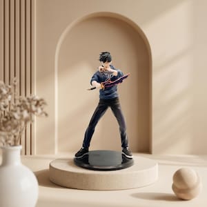 May include: A collectible anime-style figurine of a character with black hair, wearing a dark blue long-sleeved shirt and black pants. The character holds a stylized sword with a dark blade and orange accents, standing on a circular black base.