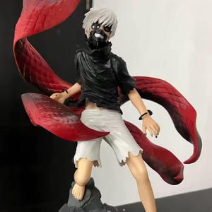 May include: A detailed figurine of a character with white hair, a black mask, and a torn black shirt. The figure has white shorts and large, red, wing-like appendages extending from the back.