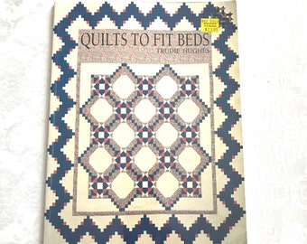 May include: A book titled "Quilts to Fit Beds" by Trudie Hughes. The cover features a quilt pattern with a blue, red, and white color scheme. The price tag is visible on the cover, showing a price of $2.98.