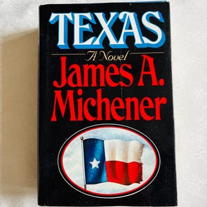 May include: A hardcover book titled "TEXAS" by James A. Michener. The cover is black with white and blue lettering. The book features an oval image of the Texas flag. The book is a novel.