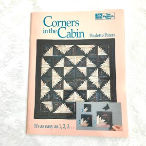 May include: Book cover for a quilting pattern titled "Corners in the Cabin" by Paulette Peters. The cover features a quilt with a black and white log cabin pattern. The text "It's as easy as 1, 2, 3..." is at the bottom of the cover.